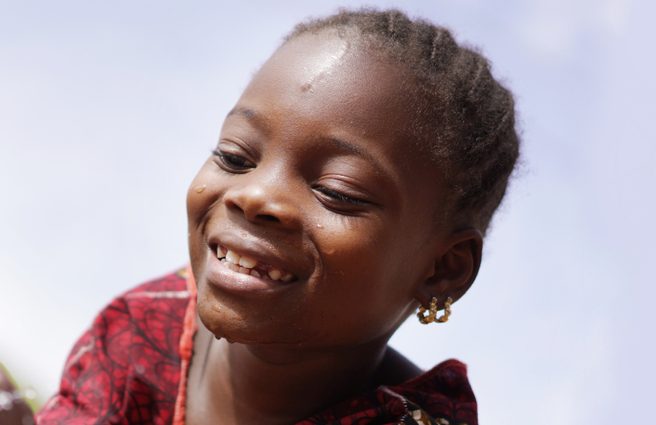 Image of a young girl smiling next to water pump