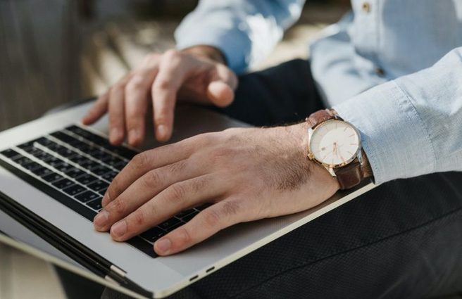 Person with blue shirt and watch typing on laptop